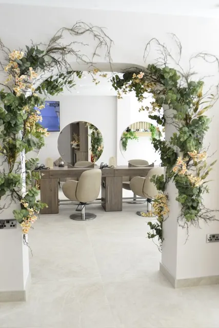 Salon with a white floor, a table with chairs, a mirror, and a wall decorated with flowers and leaves