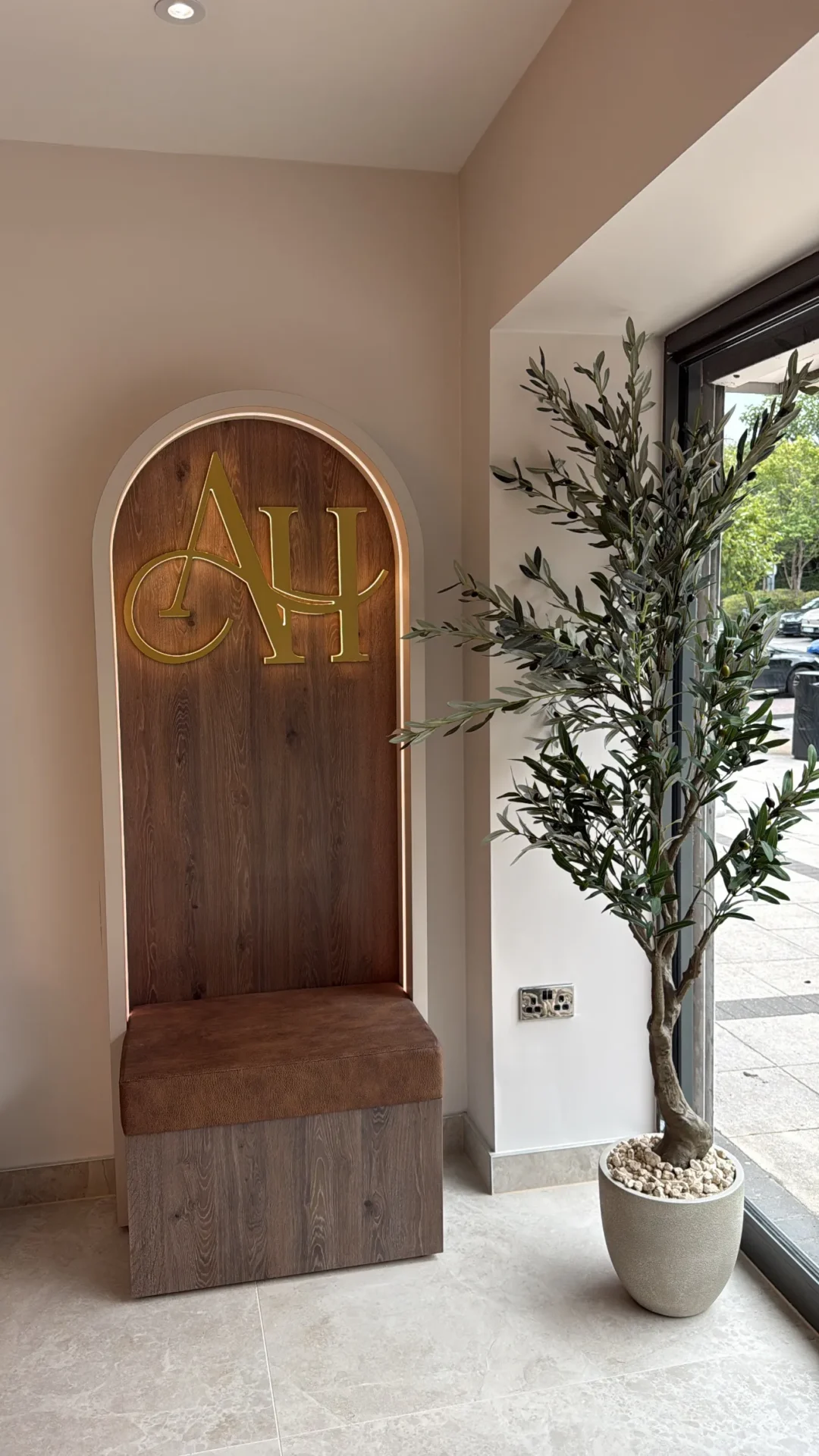 Wooden door with a potted plant in front of it, a bench, a wall, a ceiling with lights