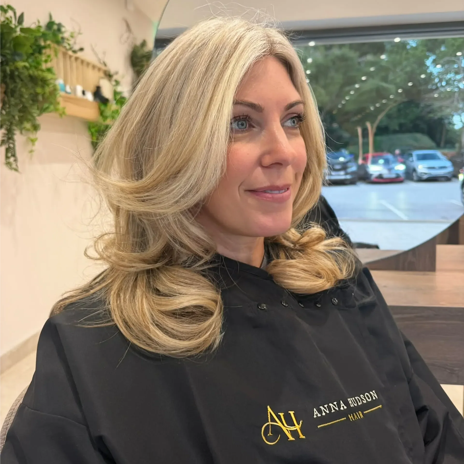 Woman sitting in a salon chair with long blonde hair, She is wearing a dress